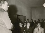  Assemblea, un militare parla a un gruppo di uomini in una sala adibita a scuola guida. 